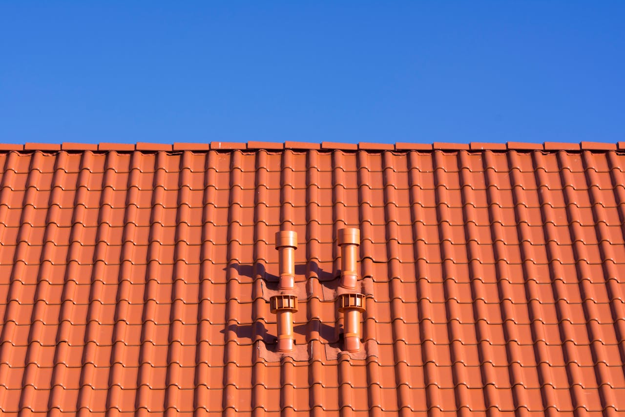 Vivid red clay rooftop with patterns and vents beneath a clear blue sky, ideal for architecture themes.